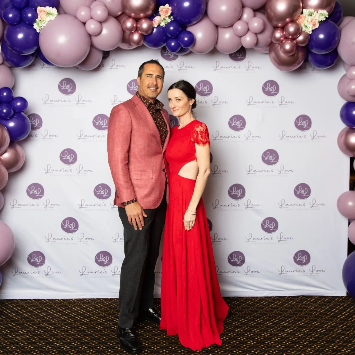 A couple posing in front of the Laurie’s Love step and repeat under a balloon arch