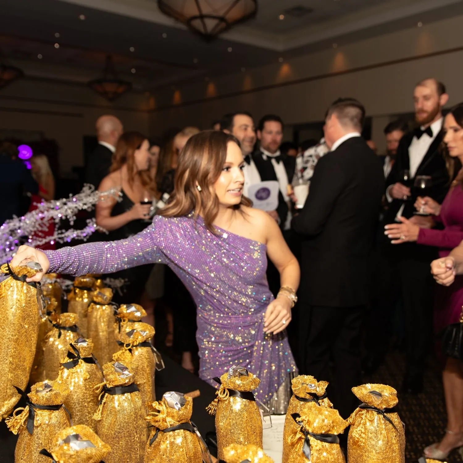 A guest in a sequin dress reaching into rows of gold gift bags