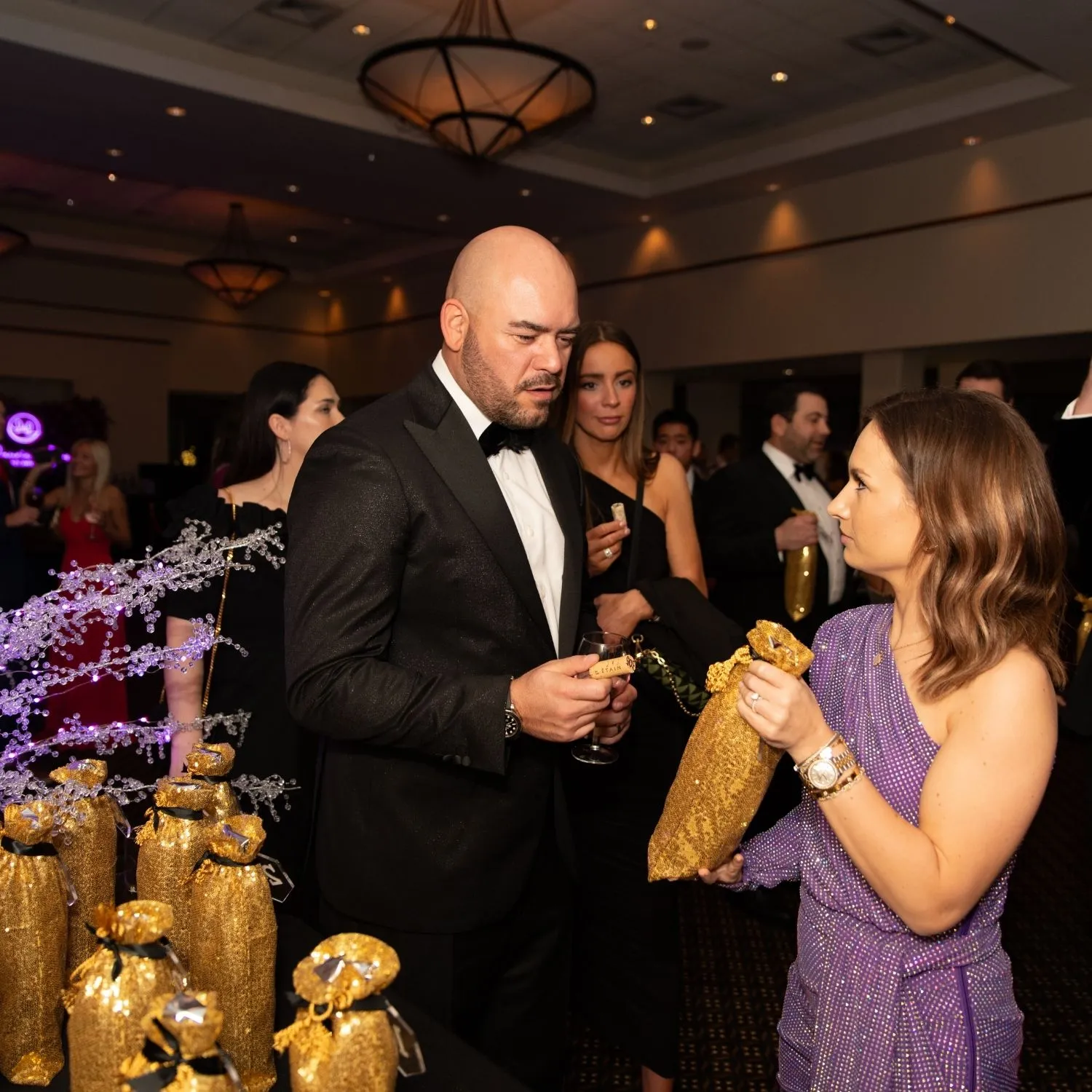 A guest in a tuxedo choosing a gold gift bag from a volunteer