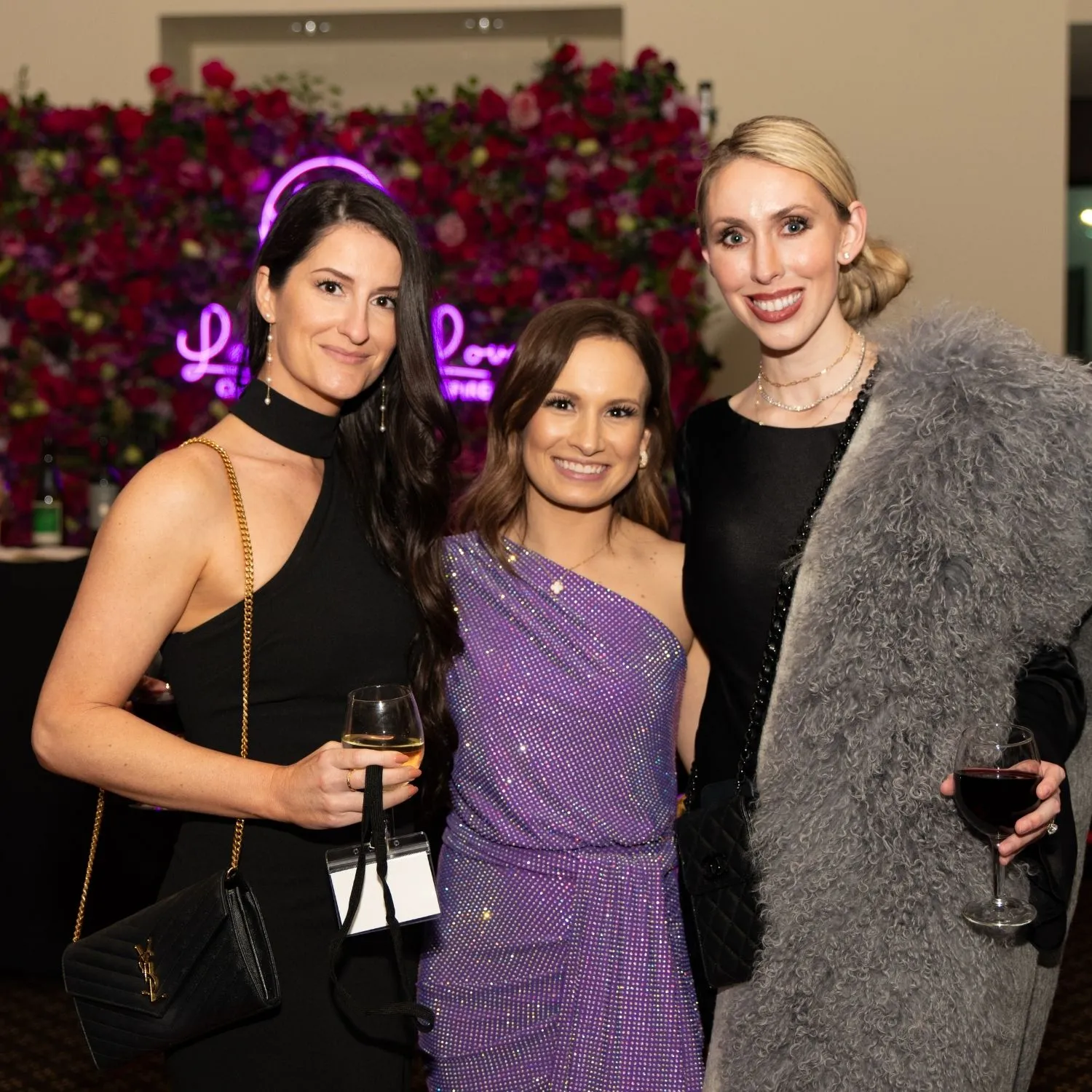 Three guests in front of a wall of roses and a neon Laurie’s Love sign