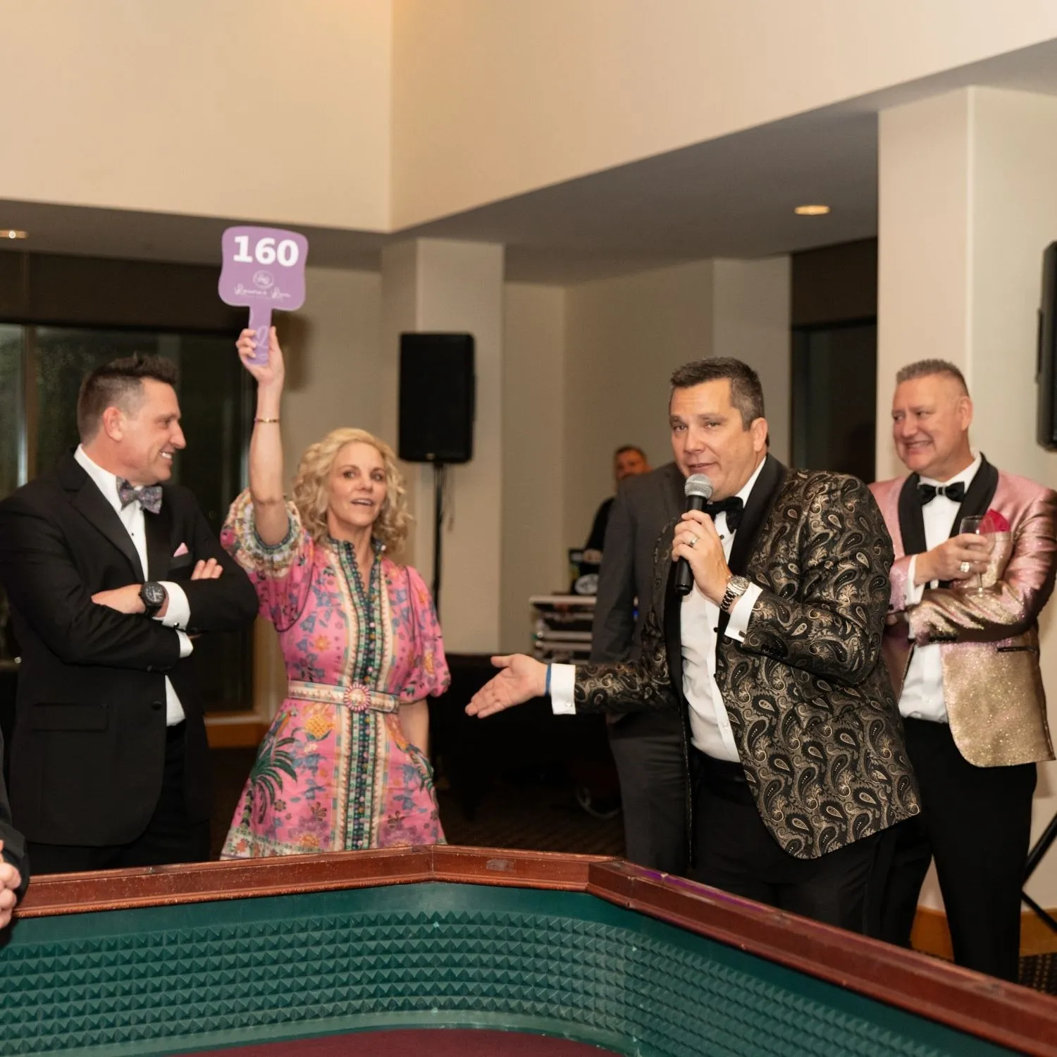 Guests cheering at the craps table, one holding up a bidder paddle
