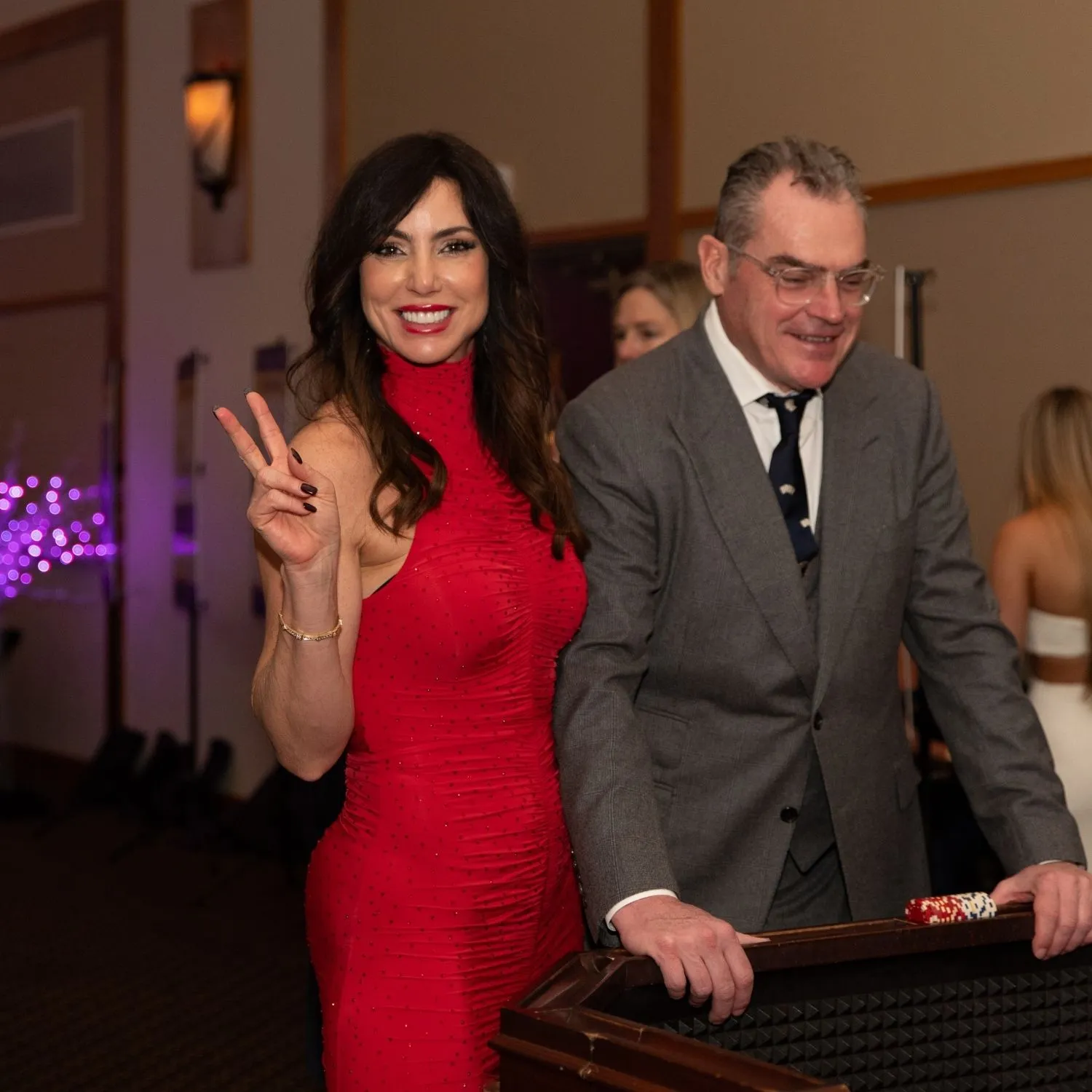 Two guests at a casino table, one flashing a peace sign