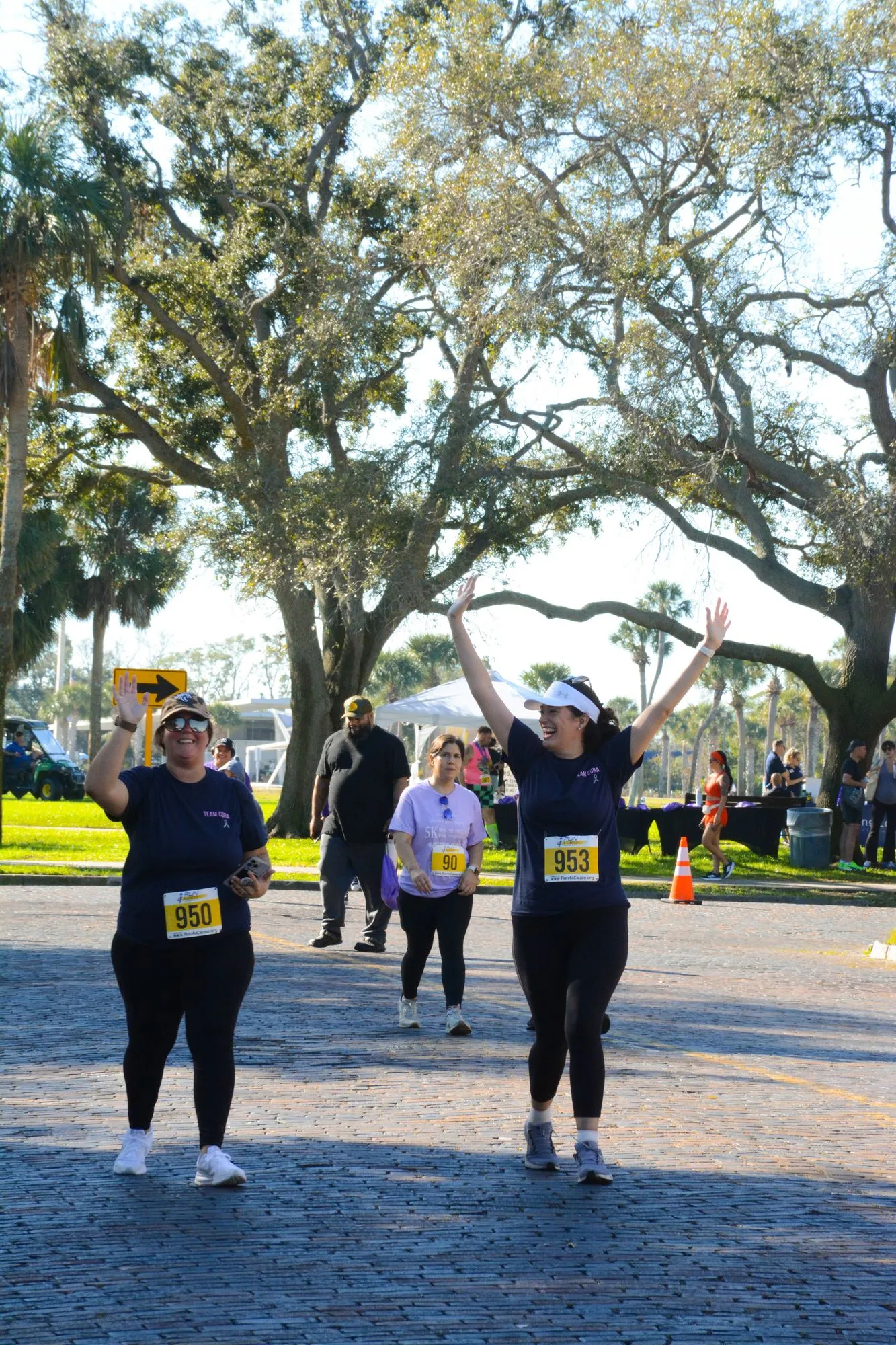 Walkers raise their arms in celebration on a brick path under oak trees at the 2026 Legacy Run