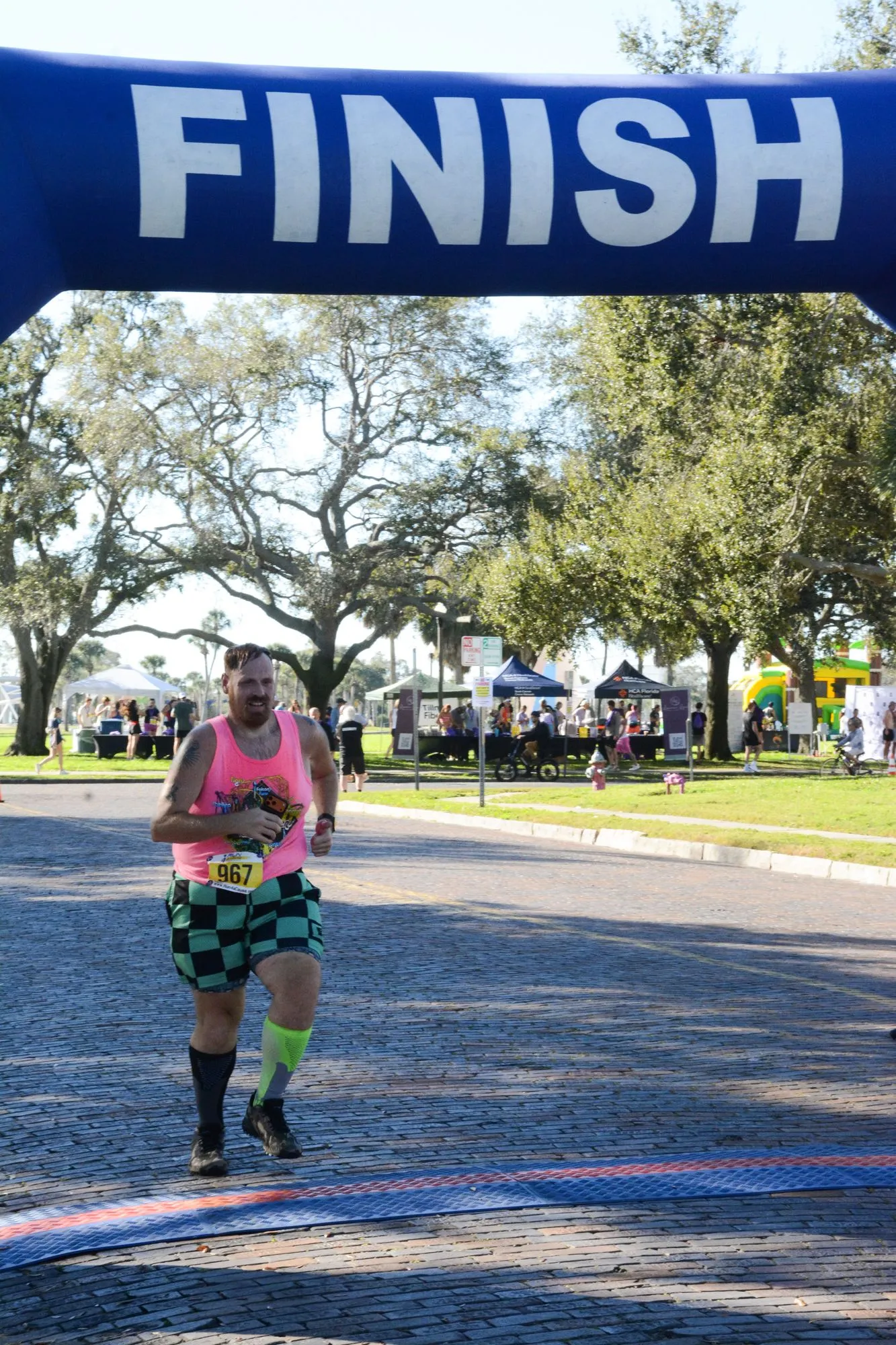A finisher in a bright pink top runs under the finish arch at the 2026 Legacy Run