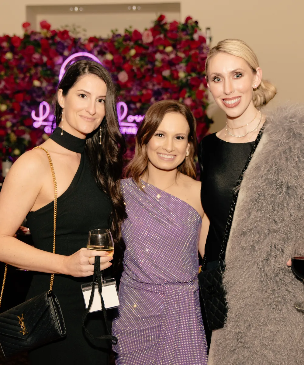 Three guests smiling together in front of a wall of roses at the 2024 Game Changer Casino Night